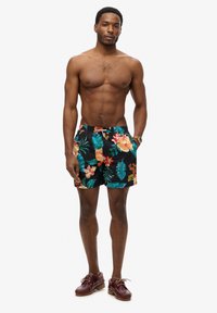 Bañador floral con un fondo negro, flores tropicales vibrantes y hojas. Cintura elástica con detalles de la marca en la parte frontal.