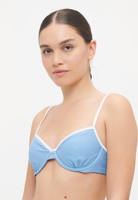 Lyseblå bikinitopp med hvit kant. Har formede kopper, justerbare stropper og samlinger nederst for ekstra tekstur.