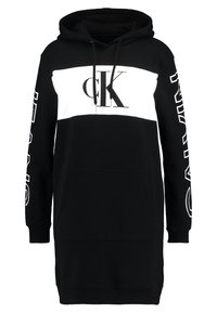 Černé mikinové šaty s bílým centrálním panelem, logo "CK" na přední straně, dlouhé rukávy se textem po straně a přední kapsou.