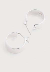 Srebrne kolczyki nausznice o wypolerowanej powierzchni, z zapięciem na zawias i gładkim, zaokrąglonym kształtem. Wykonane z metalu z subtelnym logo wewnątrz.