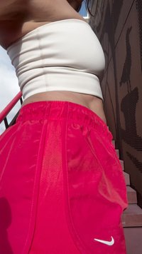 Fényes rózsaszín sportshorts, elasztikus derékkal, hálós betétekkel és egy fehér Nike logóval az oldalon. A felső részen egy testhez álló fehér top látható.