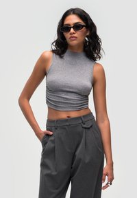 Grå, ærmeløs crop top med høj halsudskæring og samlet detalje. Parret med høj talje grå bukser med flad front og lommer.