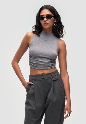 Grijze, mouwloze crop top met een hoge halslijn en geplooide details. Gecombineerd met hoge grijze broeken met een vlakke voorkant en zakken.