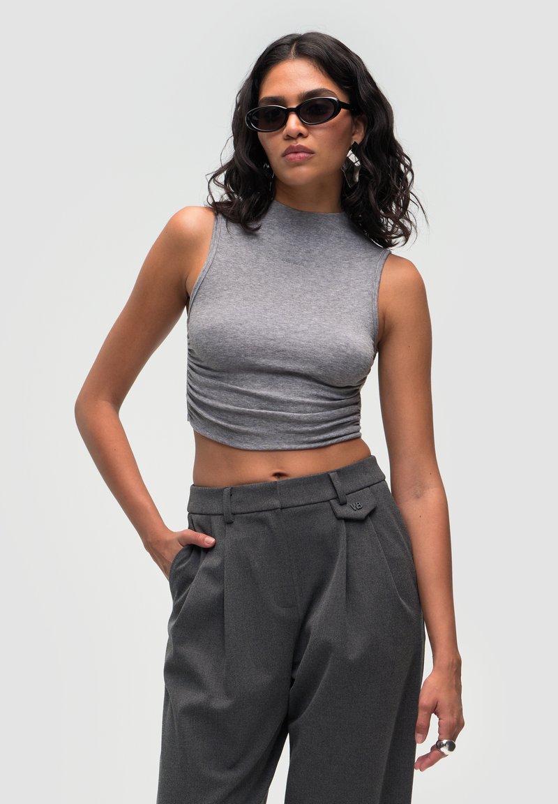 Grå, ærmeløs crop top med høj halsudskæring og samlet detalje. Parret med høj talje grå bukser med flad front og lommer.