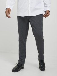 Pantalones grises de tejido suave, con un corte ajustado. Llevados con zapatos negros pulidos y una camisa blanca de manga larga con botones.