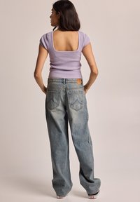 Haut court à manches courtes en lavande à côtes avec un dos carré, associé à un jean en denim bleu clair décontracté avec poches arrière et une étiquette en cuir.