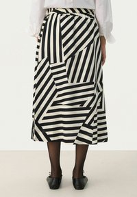 Jupe à motifs noir et blanc avec de larges rayures diagonales et horizontales, taille élastique et longueur mi-mollet. Portée avec des chaussures noires.