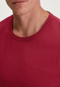 Rode katoenen T-shirt met ronde hals en een gladde textuur, met minimale stiksels zichtbaar langs de halslijn en schouders.
