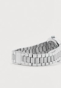 Stainless steel wristwatch band with clasp and crown, showing the back of the watch case against a plain white background.
