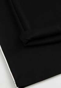 Czarny materiał rozłożony na płasko, ukazujący gładką teksturę z zagiętym brzegiem. Materiał jest gładki z kontrastującym białym stębnowaniem wzdłuż krawędzi.