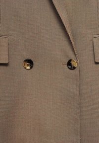 Brown houndstooth-pattern double-breasted blazer with two large buttons, notched lapels, and subtle texture on a smooth fabric surface.