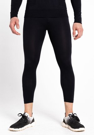 Schwarze Sportleggings aus dehnbarem Material, mit einer figurbetonten Passform und knöchellanger Länge, kombiniert mit schwarz-weißen Turnschuhen.