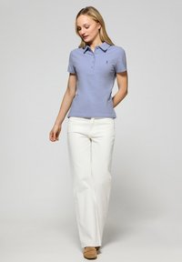 Ljust lila piké med krage och tre-knappslås, kombinerat med vita vida byxor och beige skor.