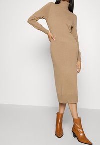 Strick, hellbraunes Midi-Kleid mit hohem Kragen und langen Ärmeln. Kombiniert mit braunen, hochhackigen Stiefeletten, die eine figurschmeichelnde Silhouette betonen.