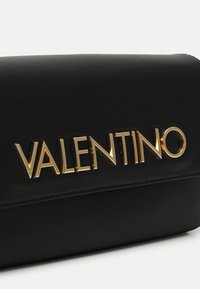 Musta nahkalaukku, jossa on näkyvä kultainen "VALENTINO"-logo, sileä pinta ja suorakulmainen muoto minimalistisilla suunnitteluyksityiskohdilla.