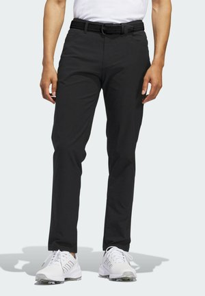 Zwarte golfbroeken met een slim fit, geweven riem en duurzame stof. Gecombineerd met witte sportschoenen met duidelijke accenten.