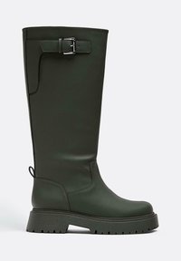 Zelená gumová vysoká bota po kolena s robustní podrážkou, zdobená stříbrnou sponou a hladkým matným povrchem. Texturovaná podrážka pro lepší přilnavost.