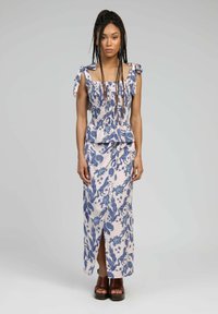 Ensemble deux pièces à motif floral dans des teintes de rose clair et de bleu, comprenant un haut smocké avec des bretelles à nouer et une jupe ajustée avec une fente sur le côté.