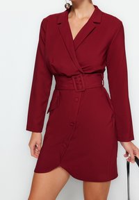Burgundy omslagsklänning med långa ärmar, bälte i midjan och sidoknappar. Tillverkad av ett mjukt tyg med en lätt lyster, med en V-ringning.