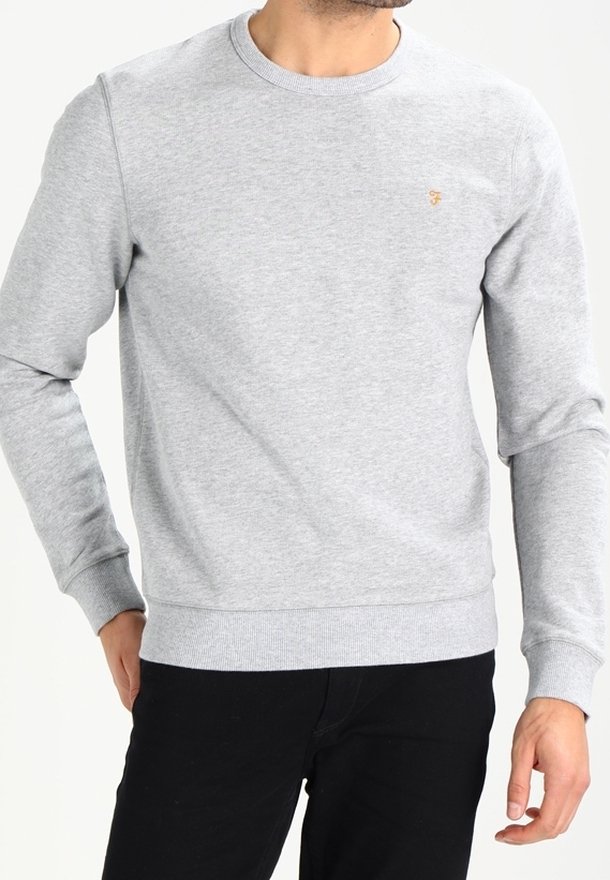 Homme portant un sweat-shirt gris clair à col rond avec manches longues et un petit logo brodé sur la poitrine, associé à un pantalon noir.