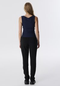 Marineblauwe tanktop met een ronde rug, gecombineerd met zwarte rechte broek. De outfit heeft een gladde textuur en een op maat gemaakte pasvorm.