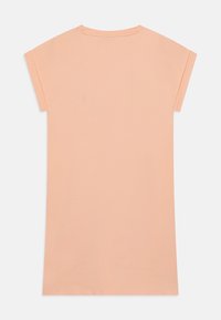 Koszulka w kolorze brzoskwiniowym z krótkimi rękawami, okrągłym dekoltem i prostym dołem. Wykonana z miękkiego materiału o gładkiej teksturze.