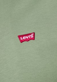 Grüner, gerippter Stoff mit einem markanten roten Levi's-Logo-Patch, das weißen Text trägt. Das Logo ist zentral auf dem Kleidungsstück platziert.