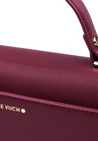 Burgunderfarbene Handtasche mit strukturiertem Design, strukturierten Oberfläche, goldfarbenen Akzenten und einem flachen Griff. Mit geprägtem Logo an der Seite.