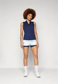 Tumesinist värvi varrukateta top, mida on kombineeritud hele siniste lühikeste pükstega, millel on tumelilla vöö. Sile kangas, istuv disain, logoga detail.