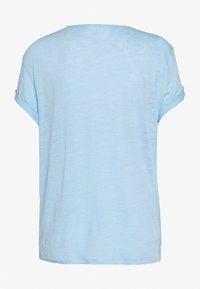 Camiseta de color azul claro, de manga corta, corte relajado, textura suave, escote redondeado, patrón jaspeado sutil, sin hardware ni acentos visibles.