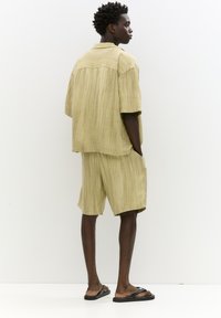 Lys khaki to-dels outfit lavet af tekstureret stof; kortærmet skjorte og knælange shorts, der har en afslappet pasform og sidelommer.