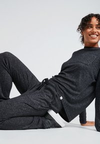 Black flecked athletic set with long sleeves and elastic waistband. Fabric appears soft, with a pocket detail on the top and sneakers.