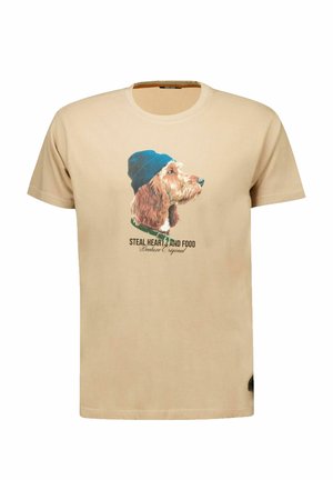 T-shirt beige à manches courtes avec un chien portant un bonnet bleu imprimé sur le devant et un texte sous le chien.