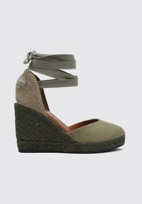 Chaussure compensée en toile verte avec un arrière beige texturé, des brides autour de la cheville et des détails en jute tissé sur le talon. Semelle en caoutchouc plate.