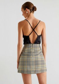 Sort satin cami med blonderkanter og krydsede stropper, parret med en tætsiddende gulternet mini-nederdel med vandrette og lodrette linjer.
