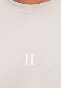Sudadera de cuello redondo en gris claro con cuello acanalado; presenta un "II" blanco impreso en la parte frontal, hecha de un tejido suave y texturizado.
