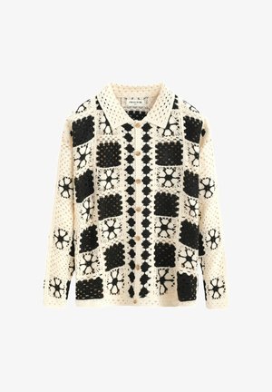 Cardigan en crochet noir et crème, présentant des motifs géométriques, un col à revers et des boutons sur le devant.