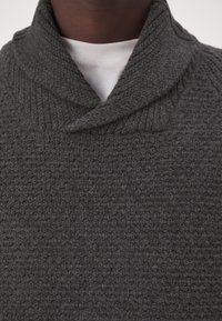 Grå, texturerad tröja med ribbad krage, som har en trattformad halsdesign. Tyget ser mjukt och fylligt ut.