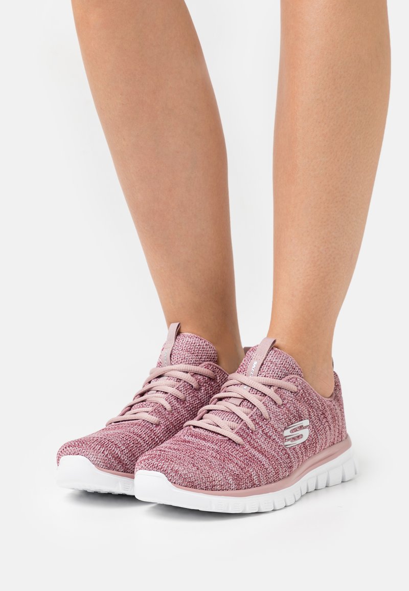 Różowe teksturowane buty sportowe z elastyczną białą podeszwą, z zapięciem na sznurówki i logotypami na zewnętrznej stronie.