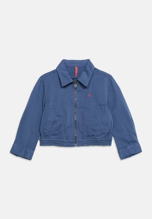 Blue cropped jacket with collar, front zipper, two front pockets, elastic waistband, and small red embroidered logo on left chest.