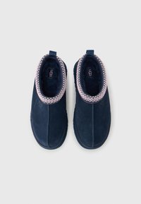 Ζευγάρι γαλάζια παντόφλες τύπου slip-on με ροζ και λευκή κεντητή διακόσμηση, μαλακή επένδυση από βελούδο και θηλιές για εύκολο φόρεμα, σε λευκό φόντο.