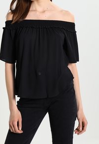 Haut noir à col bardot avec un décolleté smocké, manches courtes et coupe ample. Fabriqué en tissu léger avec une texture subtile.