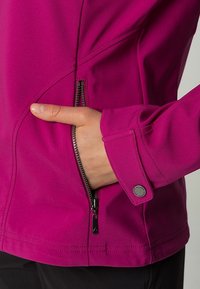 Mano dentro del bolsillo frontal con cremallera de una chaqueta morada con un puño abotonado en la manga.