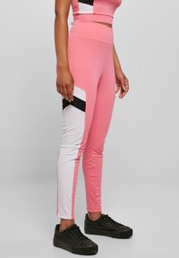 Høyhælte rosa leggings med svarte og hvite sidede detaljer, laget av elastisk materiale, tettsittende design og en jevn tekstur.