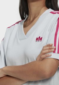 Witte v-hals t-shirt met roze schouderstrepen. Voorzien van geborduurd logo in roze en wit. Zacht, lichtgewicht stof met een relaxte pasvorm.