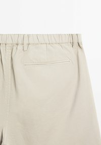 Beige bomuldsbukser med en samlet elastisk talje, en enkelt baglomme og glat tekstur. Ingen synlige mønstre eller detaljer.