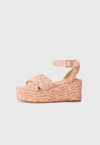 Sandale à talon compensé en rose doux, avec un dessus en paille tressée, des brides croisées, une sangle de cheville réglable et une semelle de plateau texturée.
