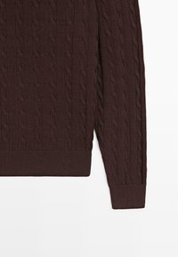 Brauner, gestrickter Pullover mit Zopfmuster, gerippten Bündchen und Saum. Das Material ist strukturiert mit einem gleichmäßigen Gewebe.