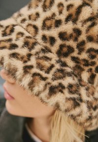 Leopard-print bucket hat made of soft, textured fabric with brown and tan tones, featuring a wide, fuzzy brim.