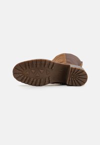 Brown rubber outsole with a patterned tread featuring triangular and rectangular shapes, complemented by a suede upper in tan and dark brown.